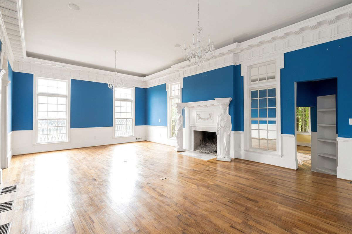 A huge blue living room with an ornate fireplace and five windows. 