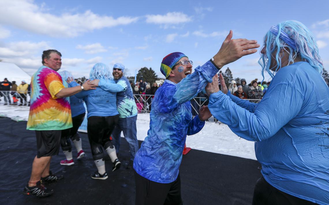 Steve Klinga (left), Jeff Crosby (third from right) and Travis Hill (second from right) of UnitedHealth Group stay in the cold after taking the Duluth Plunge to greet people in their group after their jumps Saturday on Park Point. (Tyler Schank / tschank@duluthnews.com)