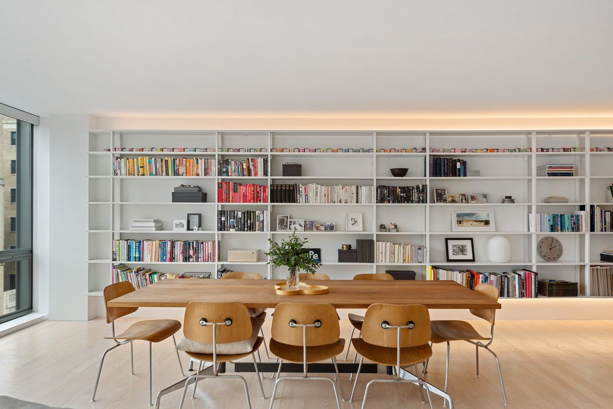A wood dining table surrounded by eight chairs in front a wall of floor-to-ceiling built-in bookshelves. 