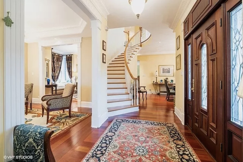 A grand foyer with a large wood door leads to sitting area and a curving staircase leading upward.