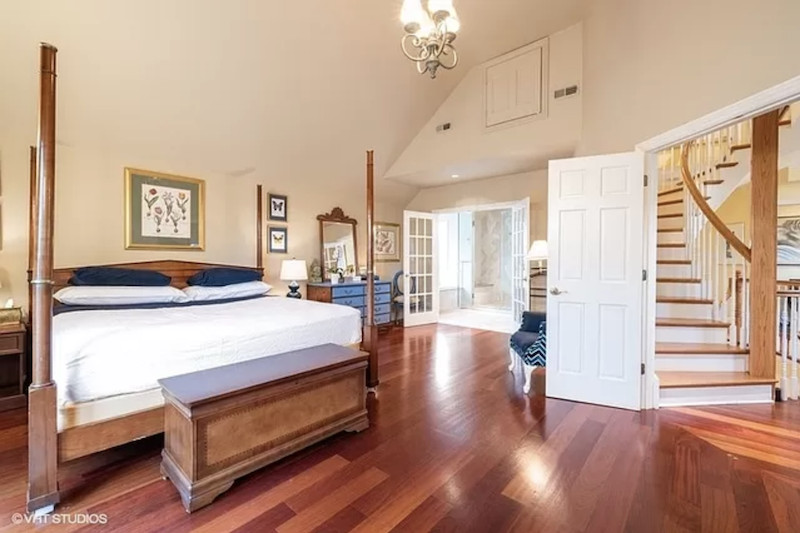 A master bedroom with hardwood floors, an attached bathroom, and a four-post bed.
