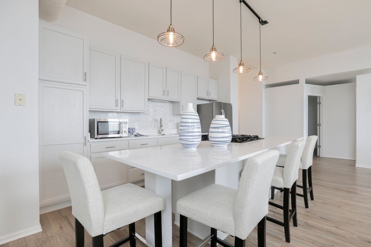 A kitchen with white cabinets, white stone counters, four pendant lights, and four high-back stools. 