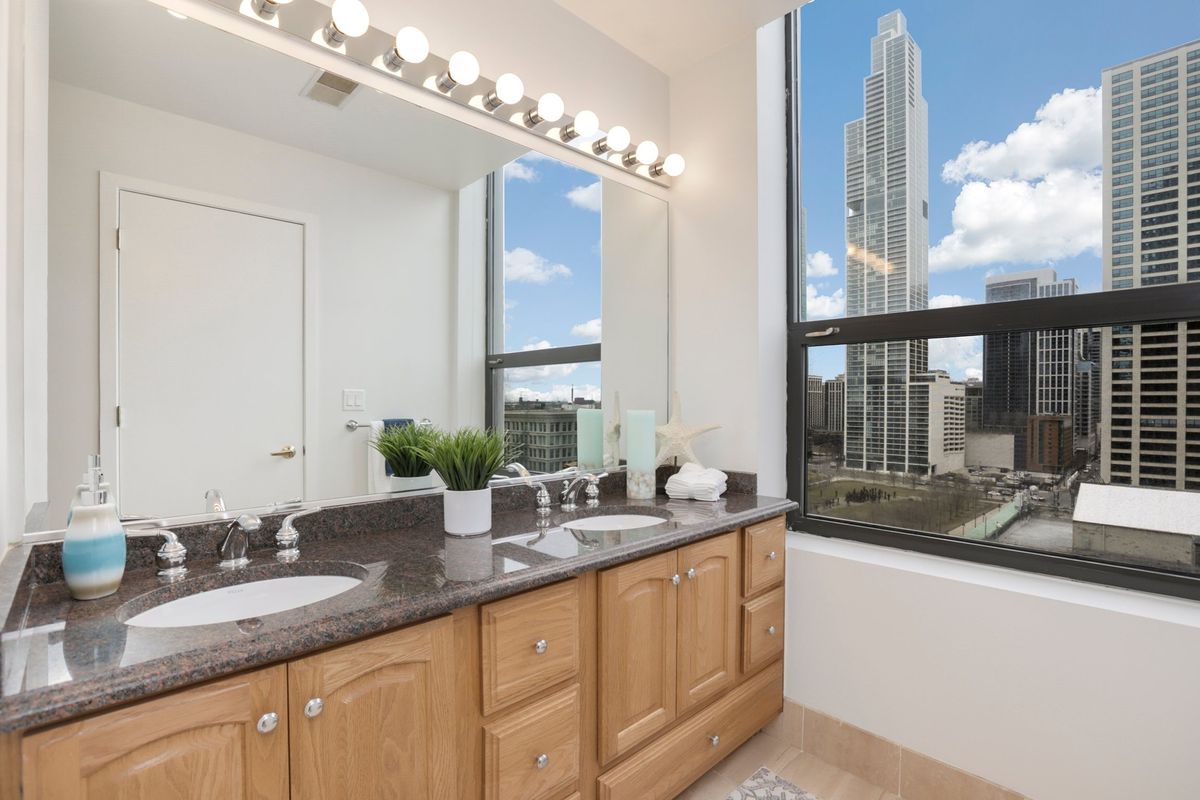A double vanity sink in front of a large mirror. Tall buildings and a park can be seen out the window.