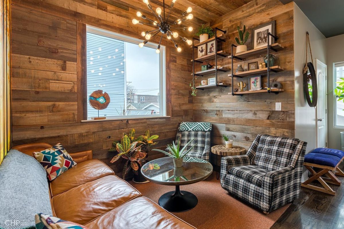 A sitting nook lined with rustic reclaimed wood has a leather couch and two plaid chairs. 