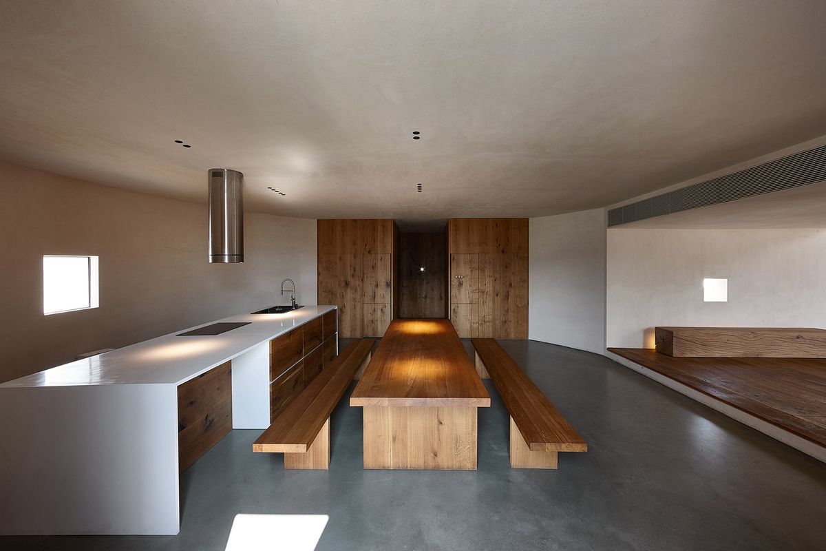 Long wooden table in kitchen with polished concrete floors.