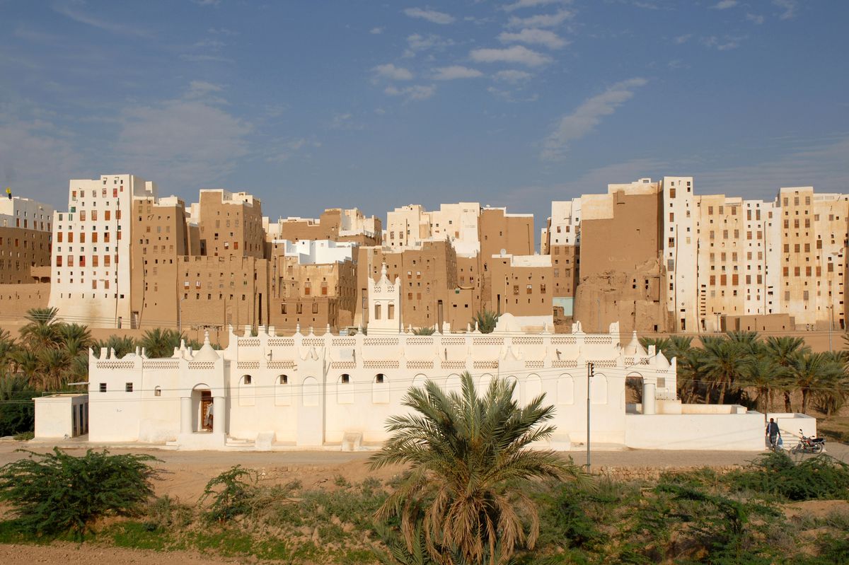 A long, white building with minarets in front of sand-colored, densely packed, multi-story homes.