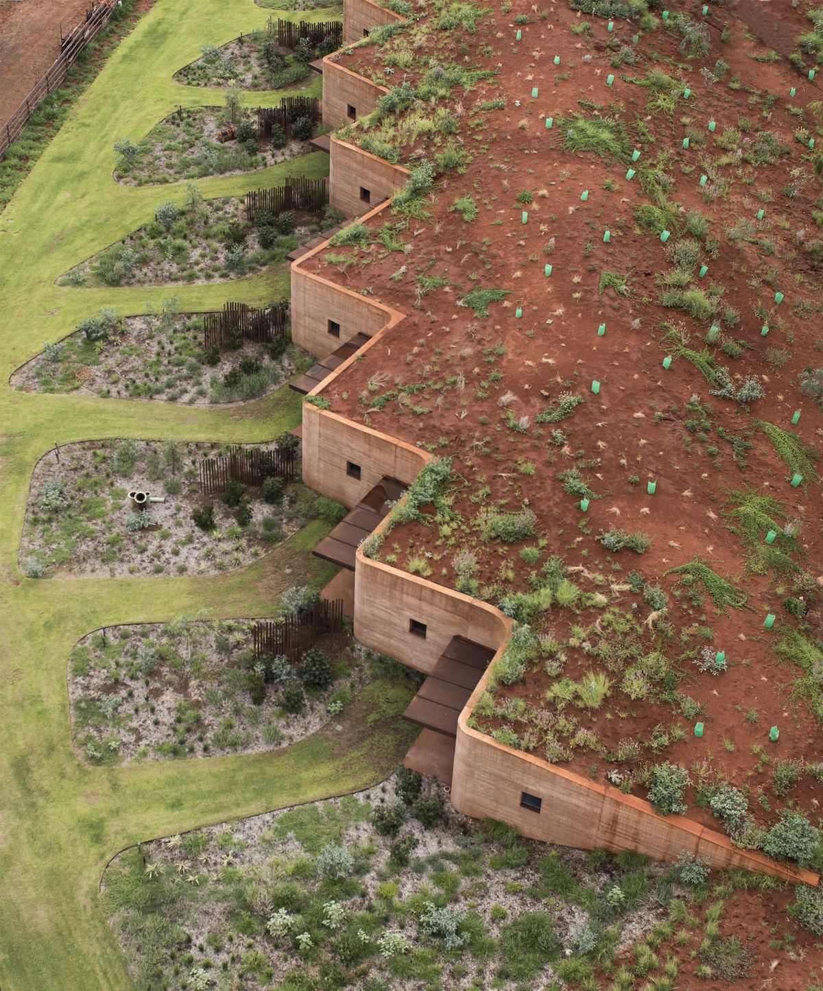A zig-zagging wall made of red earth that’s built into a hillside.