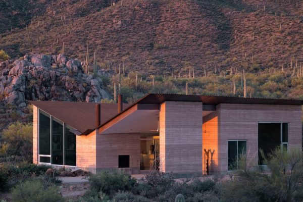 A modern home with a corrugated metal butterfly roof and earthen walls set in the desert.