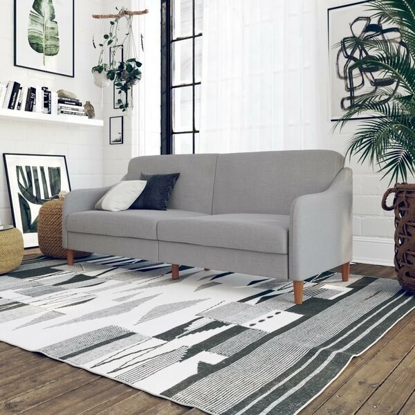 A gray sofa with attached cushions and flat arm rests, all edges are rounded and the legs are wooden 