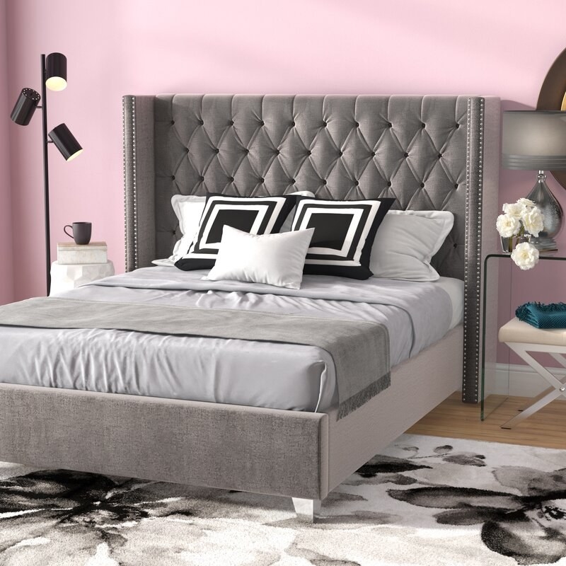 A massive platform bed with a tufted headboard that curves around each side of the bed slightly. The base matches the headboard in color and fabric and the legs are clear. 