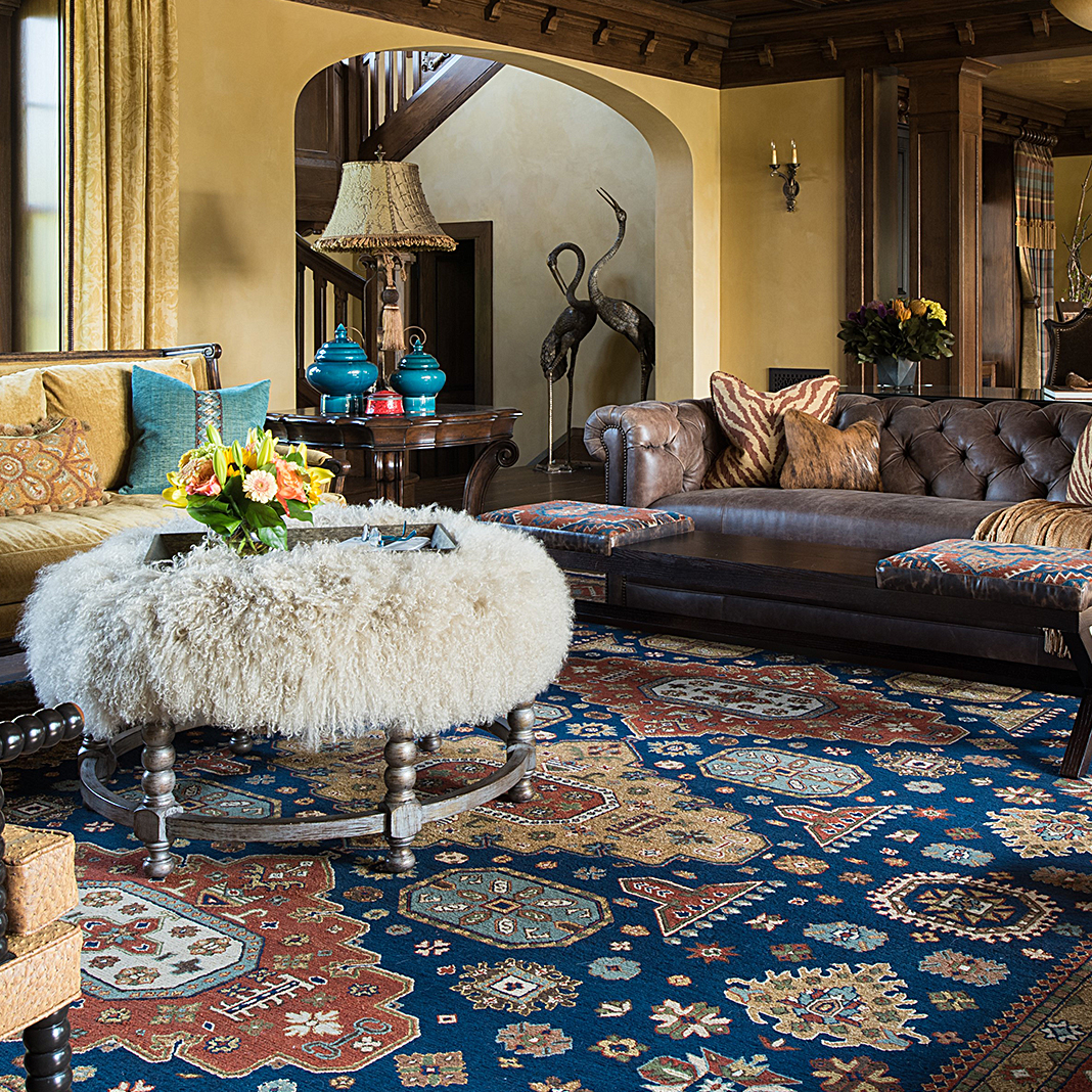 Living room with leather couches, fur covered coffee table, and an ornately designed orange and blue rug from Cyrus Artisan Rugs