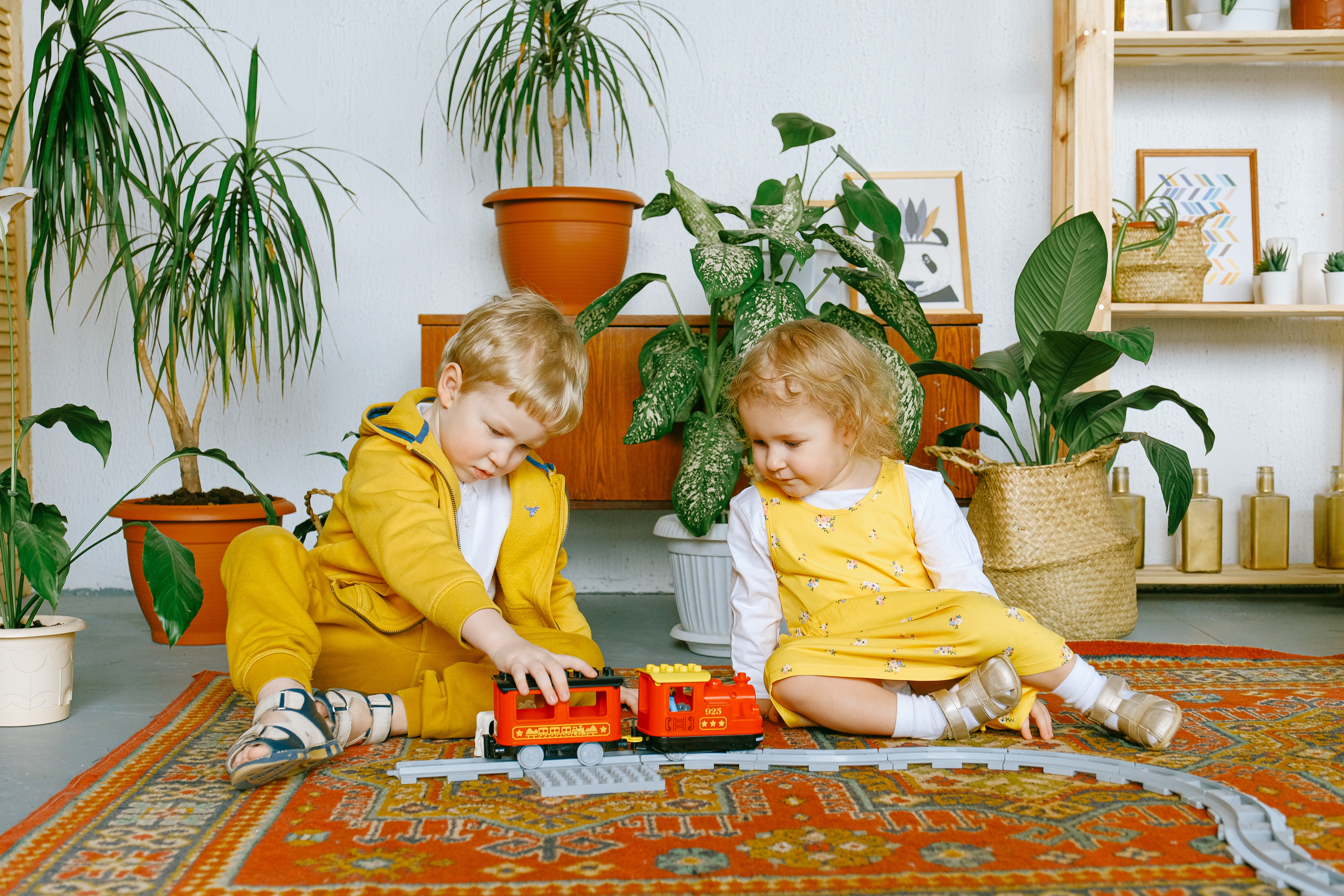 Little boy and girl sitting on the floor playing with toy train set.